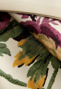 Tessuto floreale con foglie viola e verdi impreziosite da accenti gialli su uno sfondo crema. Texture liscia, design a strati.