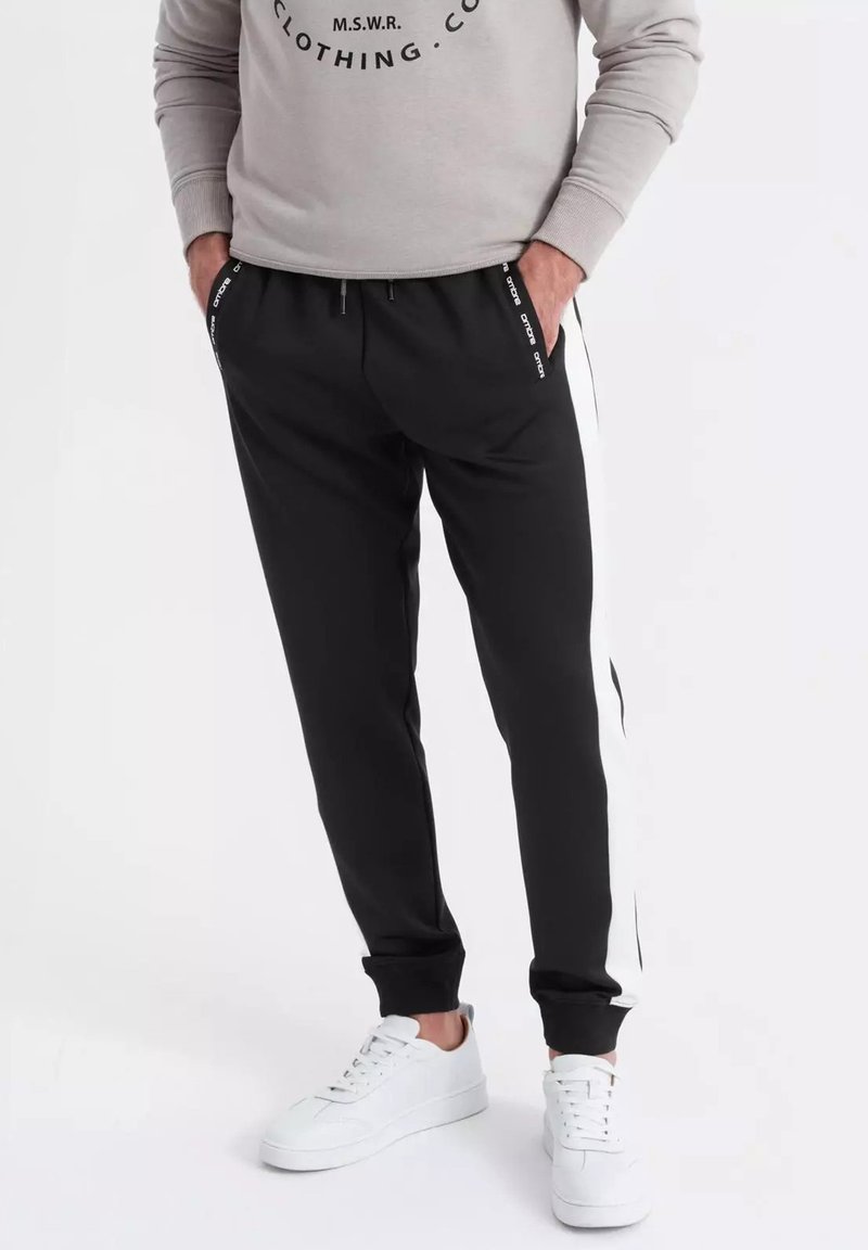 Zwarte sweatpants met witte zijstrepen, elastische tailleband en trekkoord. Gepaard met witte sneakers. Katoenmix stof.