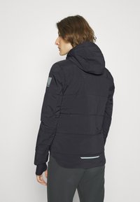 Navyblauer Puffer-Jacke mit Kapuze, gepunktetem Design, elastischen Bündchen und einem seitlichen Etikett. Der Stoff erscheint glatt mit mattem Finish.