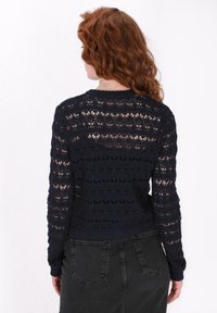 Marineblauer gehäkelter Pullover mit offenen Mustern, langen Ärmeln und Rundhalsausschnitt; kombiniert mit einem schwarzen Denim-Rock.