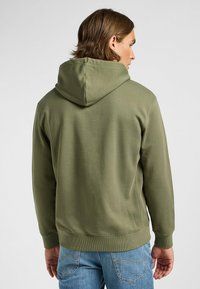 Felpa verde oliva con tasca a canguro, polsini e orlo a coste. Presenta un cappuccio con coulisse e un tessuto in morbido misto cotone.