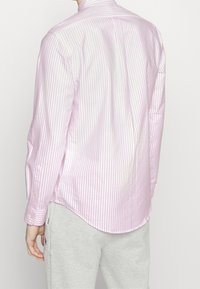 Růžová košile s dlouhým rukávem a bílými svislými pruhy, s límečkem na knoflíky a zakřiveným lemem. Nosit s šedými tepláky.