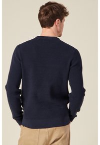 Maglione a coste con maniche lunghe, collo rotondo e fondo a costine, di colore blu navy. La texture appare morbida con una silhouette aderente.