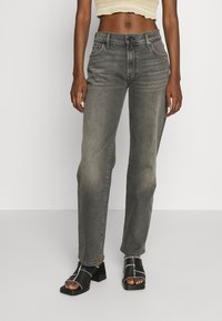 Jeans grigi alti in vita, a gamba dritta, con dettagli strappati e tasche anteriori, abbinati a sandali neri con tacco a blocco.