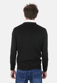 Maglione nero in maglia con design aderente e polsini a coste, indossato con jeans in denim caratterizzati da un design classico con cinque tasche e cuciture blu.