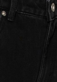 Svart denimtyg av jeans med en närbild, som visar silverfärgade metallknappar och sömnadsdetaljer längs midjan och fickorna.