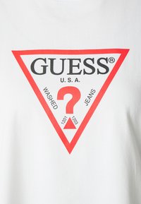 T-shirt blanc avec un grand graphique triangulaire rouge comportant "GUESS®", "WASHED", "JEANS" et un point d'interrogation au centre.