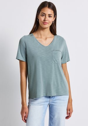 T-shirt vert clair en V, fabriqué dans un tissu texturé, avec des manches courtes et une petite poche poitrine. Coupe décontractée avec un aspect doux.