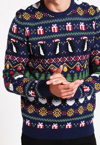 Dunkelblauer gestrickter Pullover mit festlichen Mustern, darunter Pinguine, Geschenke, Weihnachtsmann-Gesichter und Weihnachtsbäume in verschiedenen Farben.