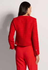 Rode cropped jacket van een textuurstof met lange mouwen en zilveren knopen. Gecombineerd met bijpassende rode broek, wat een uniform kleurenschema laat zien.