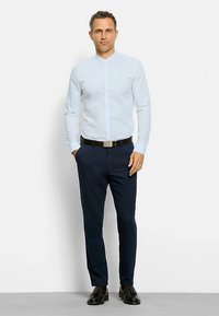 Camicia azzurra a maniche lunghe con collo alla coreana, abbinata a pantaloni blu scuro e scarpe nere, completata da una cintura nera.