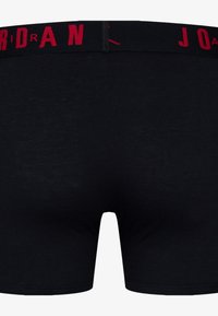 Schwarze Boxershorts mit einer weichen, glatten Textur; ausgestattet mit einem roten elastischen Bund, auf dem "JORDAN" in fetten Buchstaben eingeprägt ist.
