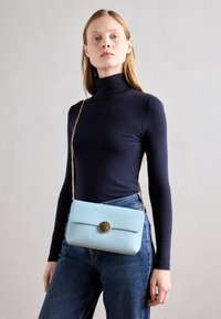 Světle modrá kožená crossbody taška s klopou a kulatým kovovým knopem, vybavená zlatým řetízkem a hladkým povrchem.