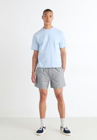 Light blue short-sleeve t-shirt paired with gray striped shorts. The outfit features a relaxed fit, crew neck, and athletic shoes.