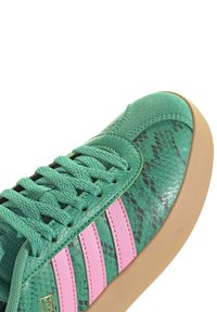 Sneaker verde con texture in pelle di serpente, design a tre strisce rosa, punta tonda e suola in gomma beige. I lacci sono dello stesso verde.