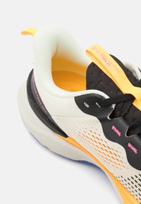 Chaussure de sport légère avec un dessus en mesh blanc respirant, des accents noirs et orange, et une semelle texturée pour une meilleure adhérence.