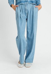 Pantaloni in denim azzurro chiaro a vestibilità ampia con frontale plissettato, due tasche laterali e una finitura texturizzata. Abbinati a ballerine argento brillanti.