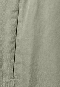 Olijfgroene stof met een fijne keperstructuur, met een gladde afwerking, opvallende naaddetails en subtiele glans.