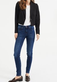 Black fitted blazer with long sleeves, worn over a white shirt, paired with dark blue skinny jeans and patent leather loafers.