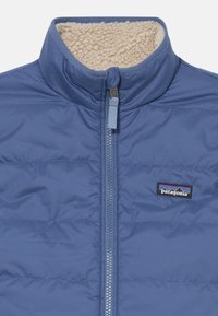 Insulated blue zip-up jacket with a high collar, soft beige fleece lining, and a Patagonia logo on the left chest. Smooth outer texture.