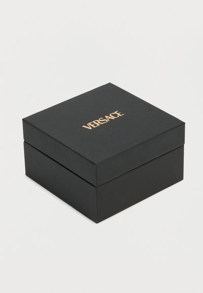 Cutie pătrată neagră cu logo-ul "VERSACE" aurit centrat pe capac, așezată pe o suprafață albă simplă.