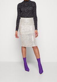 Glittrande blyertskjol i silver, åtsittande design. Svart långärmad topp med vita mönster. Lila ankelskortsstövlar med spetsig tå.