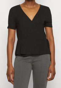 Černý top se krátkými rukávy, v-výstřihem, jemným peplum lemem a detailem s bočním vázáním. Vyrobeno z měkké a elastické tkaniny pro pohodlí.
