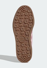 Hnědá gumová podrážka s kruhovými a listovými vzory. Obsahuje centrální logo se třemi pruhy v růžovém textilním svršku.