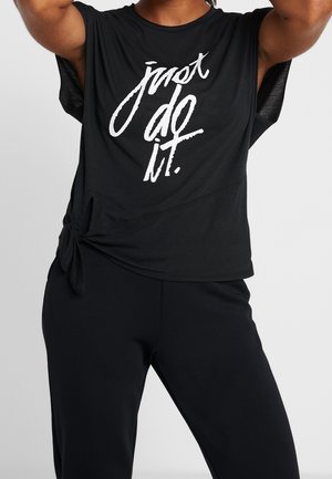 Personne portant un haut noir sans manches avec le texte « just do it. » en blanc, noué à la taille, associé à un pantalon noir.