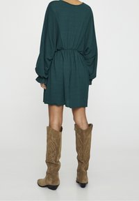 Robe texturée en bleu sarcelle avec une taille froncée et des manches amples, associée à des bottes en cuir suédé marron clair arrivant au genou avec des motifs floraux.