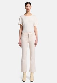 T-shirt ajusté de couleur claire avec des manches retroussées, associé à un jean flare taille haute de couleur pâle. Le modèle porte des bottines beiges.