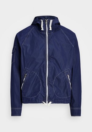 Navy blue jacket with a hood, front zipper, two front zippered pockets, and white stitching details. Lightweight material and casual design.