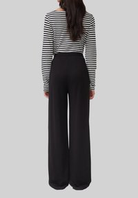 Gestreiftes Langarmhemd in Schwarz und Weiß, kombiniert mit weiten schwarzen Hosen. Die Hosen verfügen über einen elastischen Bund und eine glatte Textur.