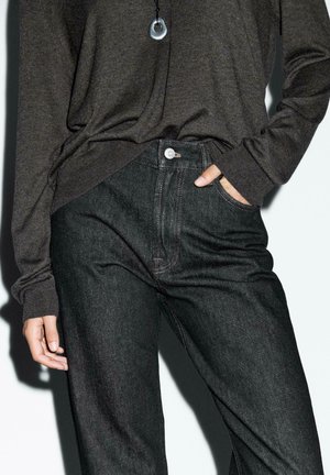 Donkerdenim jeans met een hoge taille, zichtbare stiksels en zakken, gecombineerd met een donkere lange mouw shirt. Eenvoudige ronde hanger ketting.