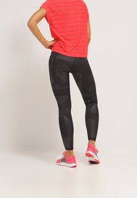 Top a maniche corte a righe rosse abbinato a leggings neri con una finitura opaca e un motivo sottile, completato da scarpe sportive rosa.