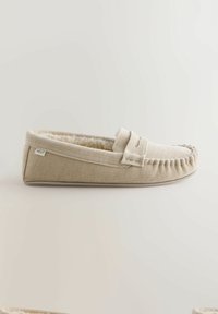 Beige moccasin pantoffel met zachte voering, gestructureerde stof en gestikte accenten. Heeft een subtiele merklabel aan de zijkant.