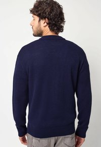 Marineblauwe gebreide trui met een ronde hals, lange mouwen en geribbelde boorden; heeft een gestructureerde stof en een relaxte pasvorm.