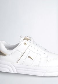 Sneaker bianco con una tomaia in pelle testurizzata, dettagli dorati e una suola bianca spessa. Presenta lacci e una decorazione con il marchio sul lato.