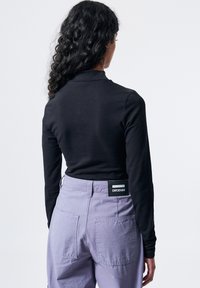 Schwarzes Langarmshirt, kombiniert mit lila Cargo-Hosen, die über zwei hintere Taschen und ein sichtbares DRDENIM-Label am Bund verfügen.
