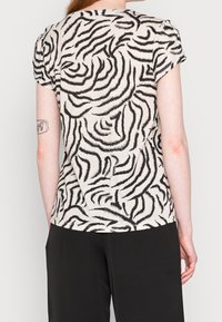 Haut à manches courtes beige avec des rayures zèbre noires, présentant une coupe décontractée et une texture douce, associé à un pantalon noir.