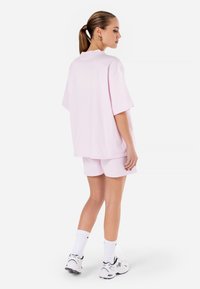 Ensemble composé d'un t-shirt surdimensionné rose et d'un short en coton ; il présente des manches courtes, une coupe décontractée et une texture lisse. Porté avec des chaussettes de sport blanches et des chaussures.