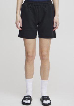 Sorte elastiske shorts med avslappet passform, laget av glatt stoff og med et enkelt design, kombinert med hvite sokker og svarte sandaler.
