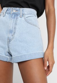 Ljusblå denimshorts med hög midja, uppvikta fållar och framfickor. Tyget har en urtvättad struktur med kontrasterande sömmar.
