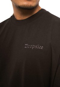 Black cotton t-shirt featuring a round neckline and a small embroidered "Dropsize" logo in a contrasting shade on the left chest.