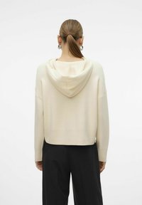 Maglione beige corto con cappuccio, orlo e polsini a costine, dal tessuto liscio. La vista posteriore mostra un design semplice e minimalista.