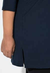 Granatowa tunika z zakrzywionym dołem i bocznymi rozcięciami, wykonana z miękkiego materiału, z krótkimi rękawami i gładką fakturą.