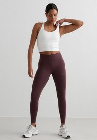 White crop top and maroon high-waisted leggings with a fitted design. Textured matte finish, with accent stitching and logo detail. White sneakers.