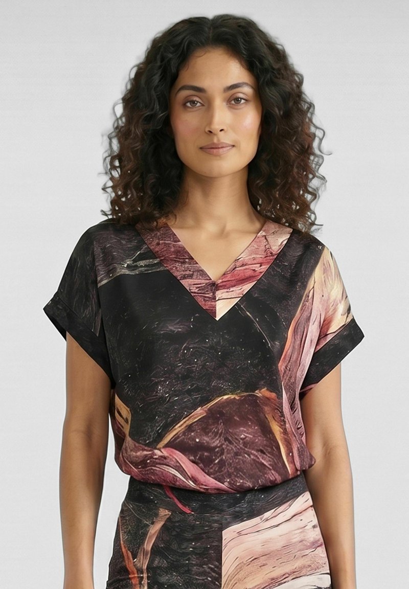 Femme aux cheveux bouclés et foncés porte un haut à manches courtes avec col en V et une jupe assortie présentant des motifs abstraits noirs, roses et marron.