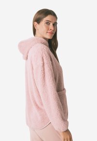 Uldet lyserøde hættetrøje med hætte og frontlomme, der har en blød tekstur og afslappet pasform, designet til afslappet brug.