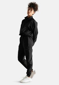 Completo sportivo nero con giacca a collo con zip e pantaloni affusolati. Abbinato a sneakers bianche. Tessuto liscio e leggero.